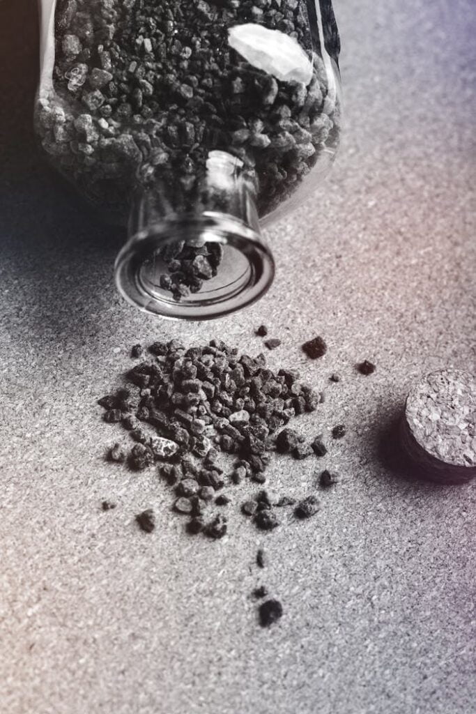 From above black and white of activated carbon granules scattered on table from glass jar with cork
